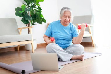 Üst düzey kadın evde egzersiz yapıyor. Dizüstü bilgisayarda antrenörü takip eden video izliyor. Spor konsepti. Kıdemli sağlık hizmetleri.