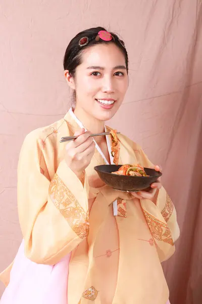 A beautiful Korean woman wearing a beautiful hanbok dress holding chopsticks is eating kimchi. Concept of Korean national costume. Fermented food