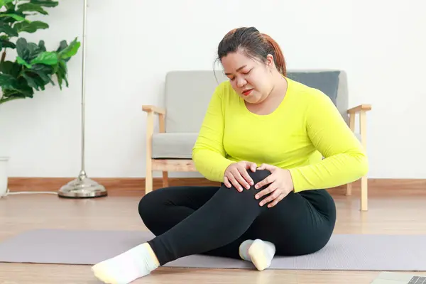 Asian fat woman sitting and exercising at home She has knee pain. Sports concept, health care. weight loss