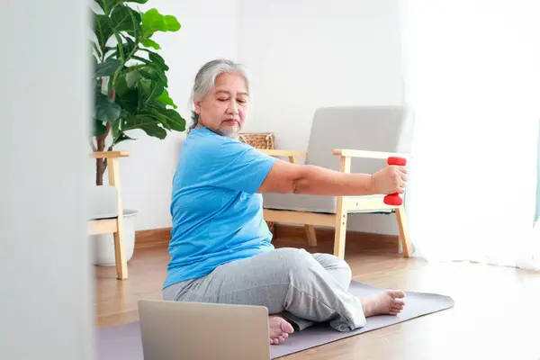 Senior woman exercising at home watching video follow trainer online on laptop computer. Sport concept. Senior health care.