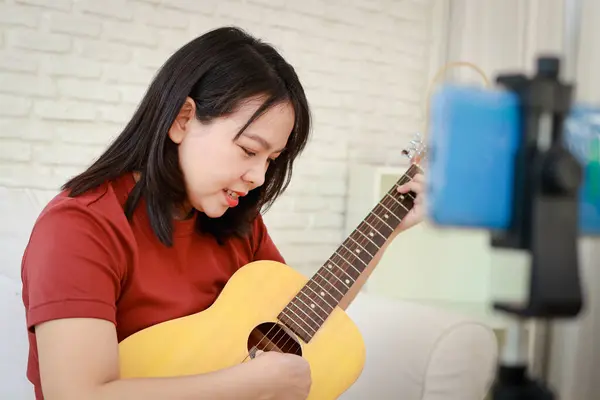 亚洲女音乐家在智能手机上在线弹吉他 在线音乐老师 国际音乐概念 图库图片