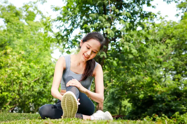 年轻美丽的亚洲女人在公园里做运动 双腿伸展在草地上坐着 体育概念 图库图片