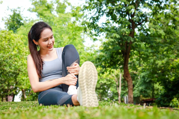 年轻美丽的亚洲女人在公园里做运动 双腿伸展在草地上坐着 体育概念 免版税图库照片