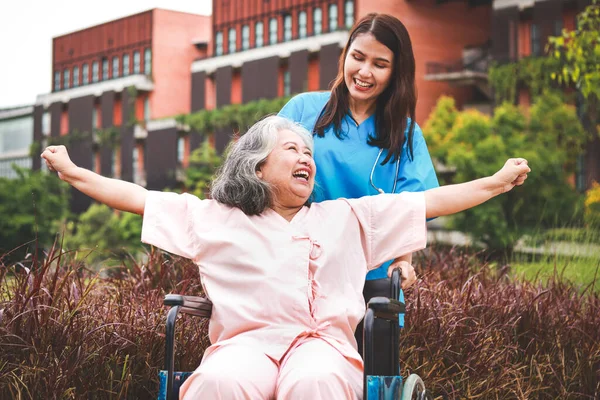 女医生穿着外科长袍 与老年女性病人一起在户外 两人都笑得很开心 医院医疗服务的概念 老年人保健 免版税图库照片