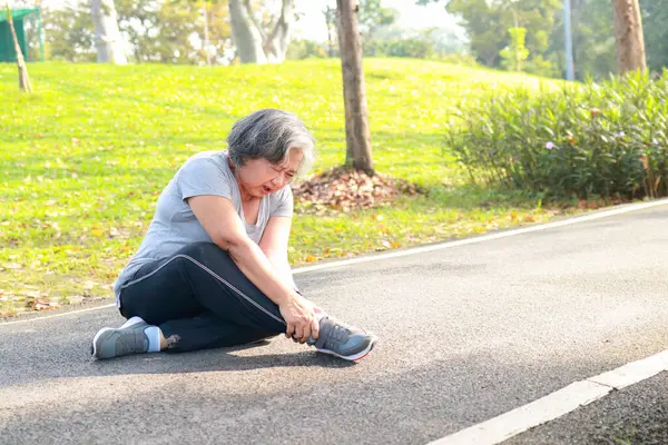 亚洲老年妇女早上在公园里慢跑 她因运动脚踝受伤 她感到很痛苦 老年人健康保健的概念 免版税图库照片