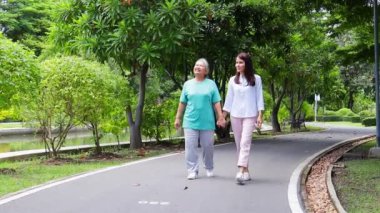 Asyalı anne ve kızı parkta birlikte yürüyüş yapıyorlar. Onların her ikisi de mutlu bir şekilde gülümsedi. Aile kavramı. Emeklilikte yaşlıların bakıcısı. Huzurevi