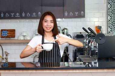 Bir kafede elinde bir kupa sıcak kahve tutan Asyalı kadın işçi işinden zevk alarak gülümsüyor. Girişimci konsepti. restoran işi