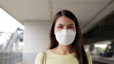 Platformda yürüyen ve tren bekleyen maske takan Asyalı bir kadının portresi. Başkentte trafik ve ulaşım kavramı. İş çıkış saatinde seyahat etmek kolaydır.