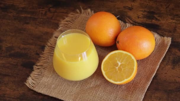 Ποτήρι Χυμό Πορτοκαλιού Και Πορτοκάλια Κοντά Ένα Τραπέζι — Αρχείο Βίντεο