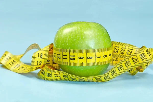 青い背景に測定テープで囲まれた緑のリンゴ — ストック写真
