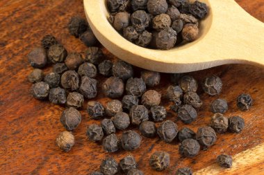 Tahta kaşıkta siyah biberler, yakın plan.