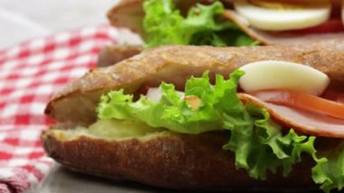 Kesme tahtasında iki jambonlu ve çiğ sebzeli sandviç.