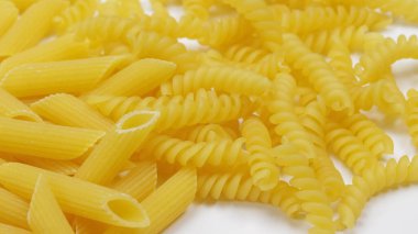 Penne makarna yığını ve çiğ fusilli, yakın plan, beyaz arka planda izole