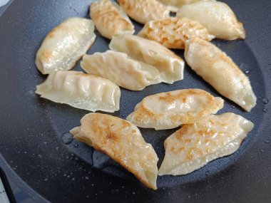 Tavada birkaç gyoza pişiyor.