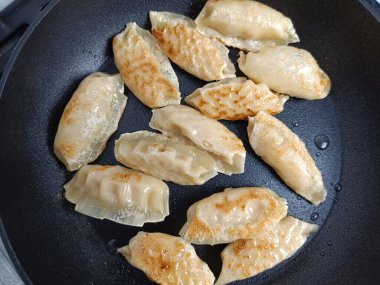 Tavada birkaç gyoza pişiyor.