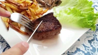 Bir insanın ellerinin bir tabakta ızgara et keserken yakın plan fotoğrafı.