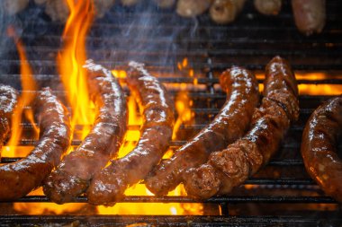 Merguez barbekü ızgarasında yemek pişiriyor, yağlar alevleri körüklüyor..