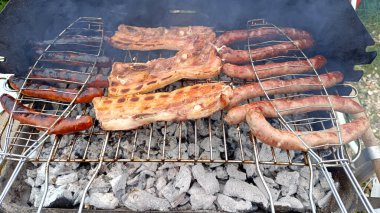 Sosisler, pastırma dilimleri ve barbeküde pişirilen merguez.