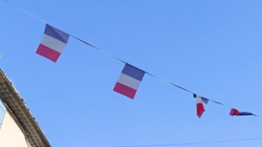 Mavi gökyüzünün altında sallanan Fransız bayrakları.