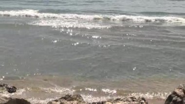 Dalgalar kumlu ve kayalık bir plaja geliyor.