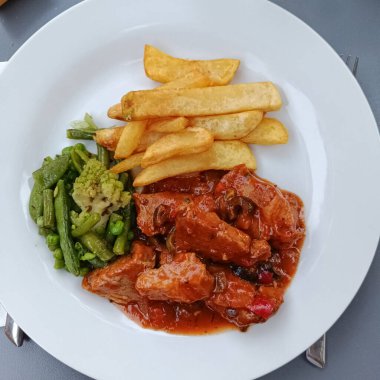 Domates sosunda pişmiş et, patates kızartması ve yeşil sebzeler.