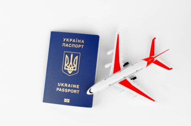 Beyaz arka planda Ukrayna pasaportu ve bulanık oyuncak uçak, üst görüş, seçici odak