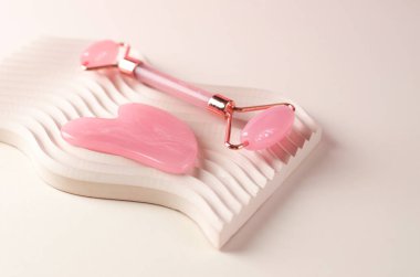 Gül kuvars guaj masajı kazıyıcısı ve sıva geometrik bir podyumda yüz masajı silindiri. Yaşlanma karşıtı tedaviler