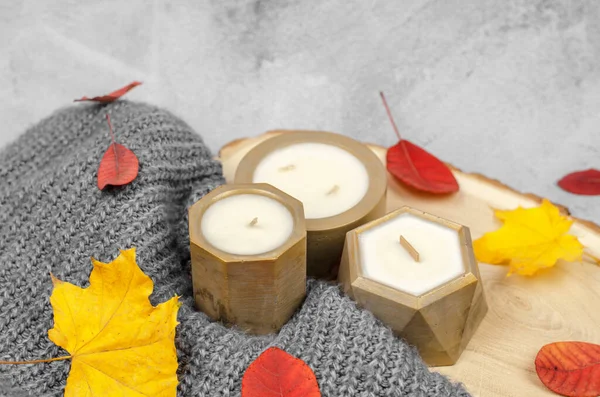 Candles in golden pots, red and yellow autumn leaves, minimal composition. The concept of home warmth and comfort