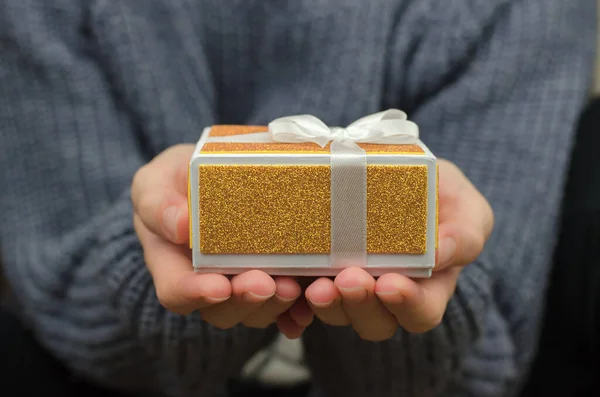 woman holds a small gift box, close-up. Woman with golden gift box