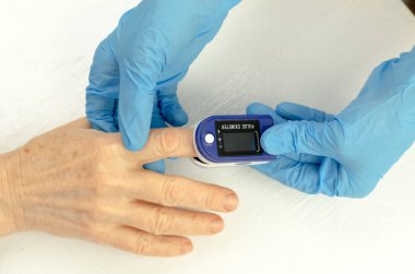 Tıbbi eldivenli bir doktorun elleri yaşlı bir Çinli kadının parmağına nabız oksimetresi uyguluyor. Yaşlıların sağlığıyla ilgilenmek.