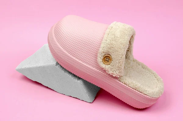 Warm room slippers with fur on a stone, pink background