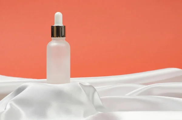 White cosmetic bottle on silk fabric. Bottle of cosmetic serum or essential oil