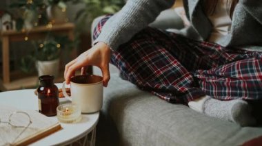 Sıcak kadın bacakları örülmüş sıcak çorap ve damalı pijama giyip sıcak kakao ya da kahve içerek evdeki kanepede oturuyor. Mum, dekor, kurabiye ve kapalı alan bitkileriyle sonbahar titreşimleri