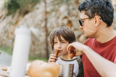 Babasının yakın çekim görüntüsü, dağlarda bir aile pikniğinde okul oğluna sarılıyor. Çocuk ve babası dağlarda yürüyüş yaparken dinlenip pikniğin tadını çıkarıyorlar..