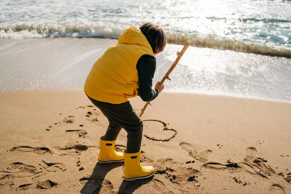 Boy Yellow Rubber Boots Drawing Heart Shape Sand Beach School — Fotografia de Stock