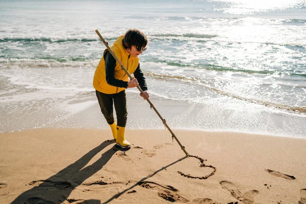 Boy Yellow Rubber Boots Drawing Heart Shape Sand Beach School — Fotografia de Stock