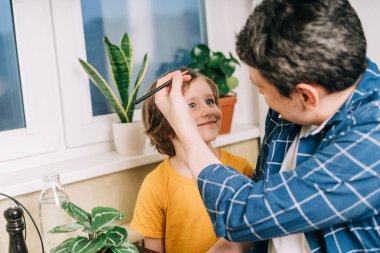 Easter day. Male Father and son painting eggs on wooden background. Family sitting in a kitchen. Preparing for Easter, creative homemade decoration. Child kid boy having fun and painting easter eggs