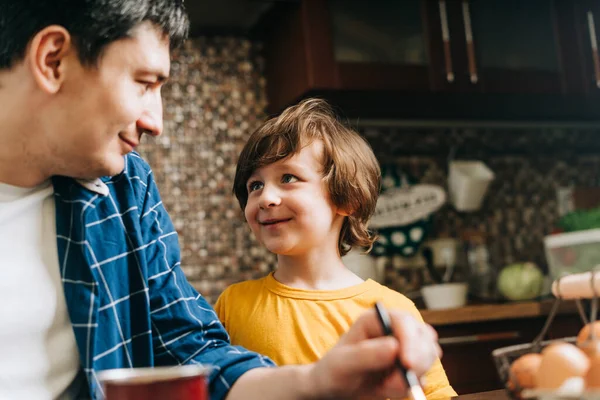 Easter day. Male Father and son painting eggs on wooden background. Family sitting in a kitchen. Preparing for Easter, creative homemade decoration. Child kid boy having fun and painting easter eggs