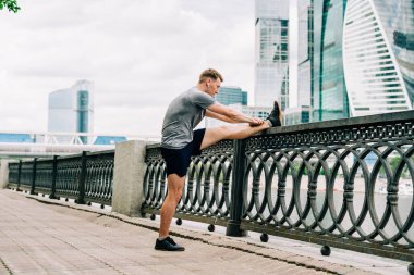 Genç fitness koşucusu şehir caddesinde egzersiz yapmadan önce bacaklarını esnetiyor. Sağlıklı yaşam tarzı ve spor anlayışı.