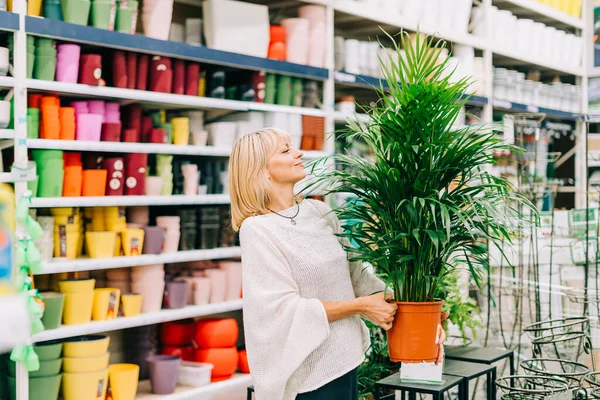 stock image Gardening, planting and shopping concept. Beautiful mature adult woman choosing houseplants and pots in greenhouse or garden centre. Senior buying flowers plants at market store in mall.