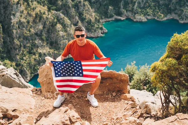 Junger Mann Sitzt Auf Einem Berggipfel Und Hält Die Flagge — Stockfoto