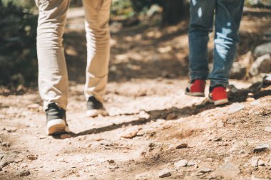 Turist topuklu ayakkabılı okul çocuğu ve babasının bahar ormanında taş patikada yürümelerini yakından izliyoruz. Çocuk ve baba yaz ormanlarında yürüyüş yaparken günlük kıyafetler giyerler..