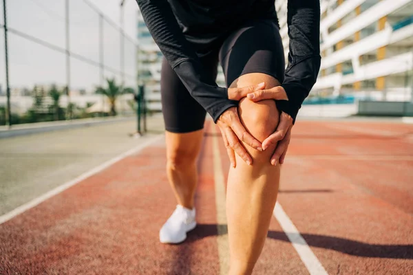 stock image Close up of sport woman holding knee with hands in pain after suffering injury running. Runner woman sit on road with knee injury and pain. 