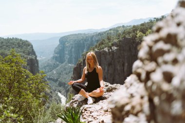 Siyah spor kıyafetli güzel bir kız uçurumun kenarındaki vadi kanyonunda meditasyon yapıyor. Uygun kadın yürüyüşçünün resmi dağın zirvesine ulaştı..