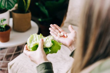 Sebze ya da tablet vitamin hapı seçen kadınların ellerini kapatın. Evde bitkileri olan bir kız, sağlıklı yaşam tarzı konsepti..
