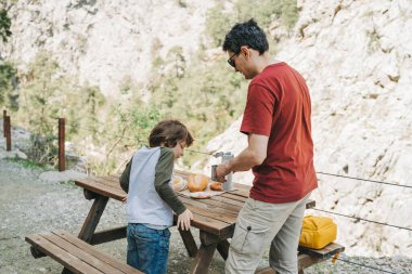 Babam dağlarda aile pikniğinde termostan fincana sıcak kahve doldurur. Çocuk okul çocuğu babasının bardağı sıcak içecekle dolduruşunu izliyor..