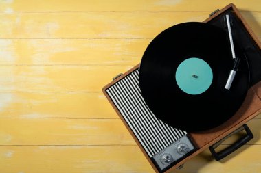 Old gramophone with a vinyl record on yellow wooden table, top view, vintage style.