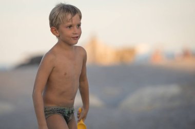 Kumsalda küçük renkli plastik oyuncaklarla oynayan küçük sarışın çocuk, eğlenceli ve aktif bir yaz tatili olan kumdan kale inşa eden çocuk..