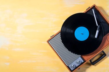 Old gramophone with a vinyl record on yellow wooden table, top view, vintage style.