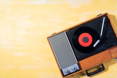 Old gramophone with a vinyl record on yellow wooden table, top view, vintage style.